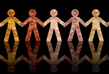 Paper cutout figures in various shades holding hands, symbolizing diversity and unity, with their reflections on a black background.