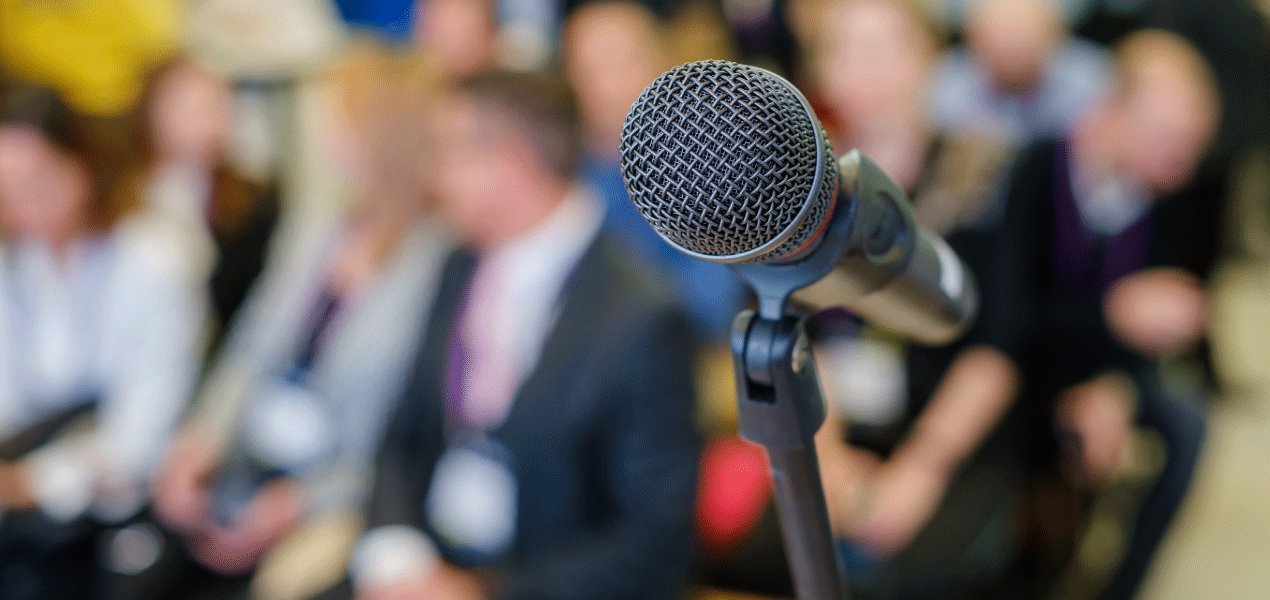 Confident professional speaker standing beside a presentation board during a business seminar or legal conference.