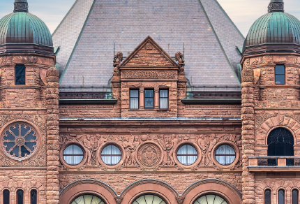 Close up photo of Queen's Park, the Ontario Legislative building, made of brown bricks with two columns, each with green roofs.