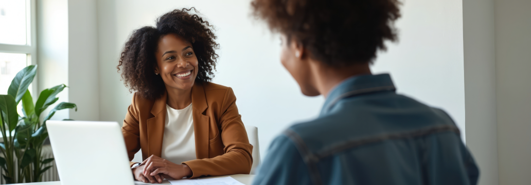 Two professionals seated across from each other at a table during a conversation in a bright office.