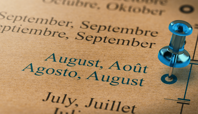 Close-up of a multilingual calendar showing the months July and August in English, French, Spanish, and German, with a blue pushpin marking July.