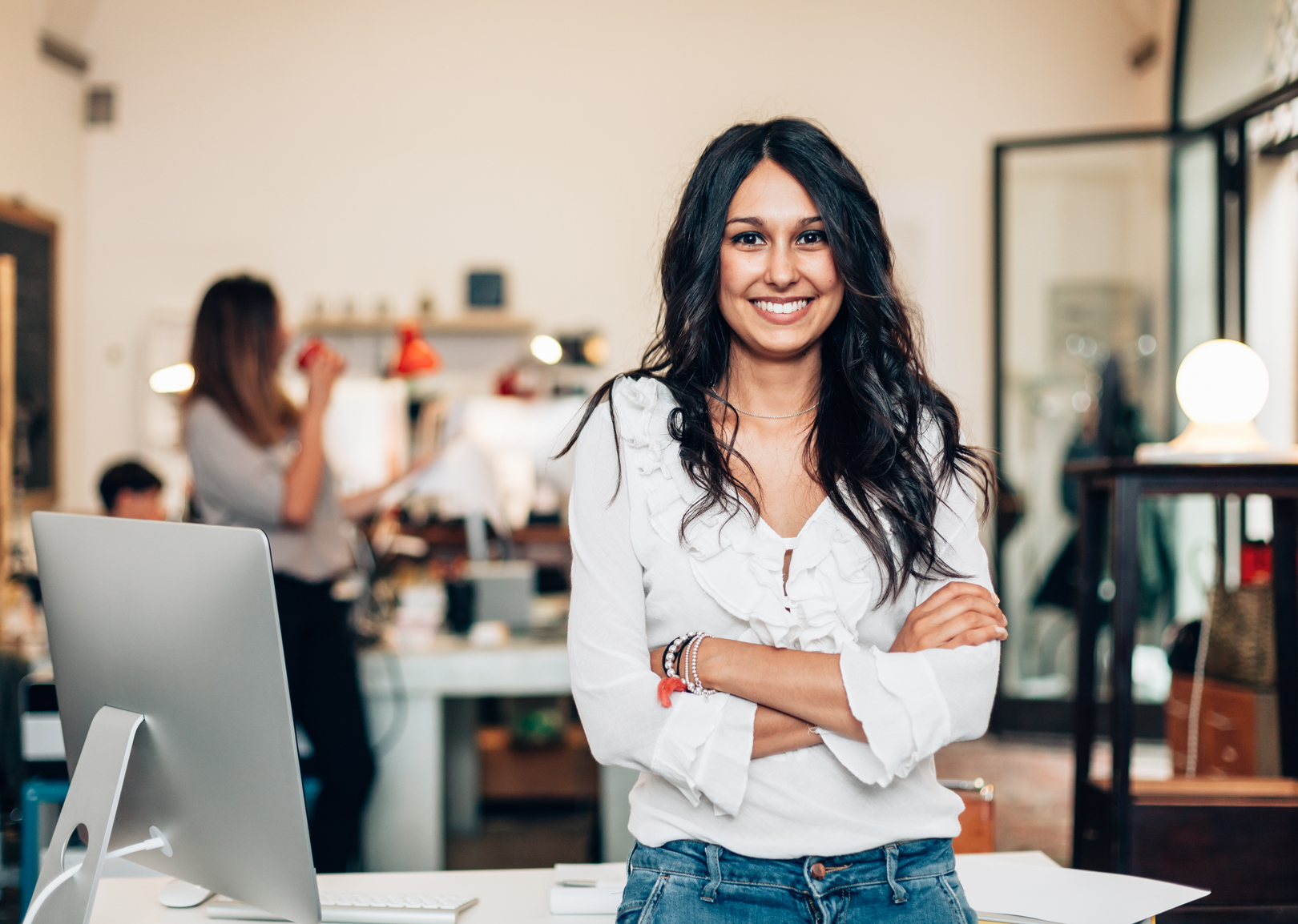 A confident female leader smiling with her arms crossed while leaning against a table.