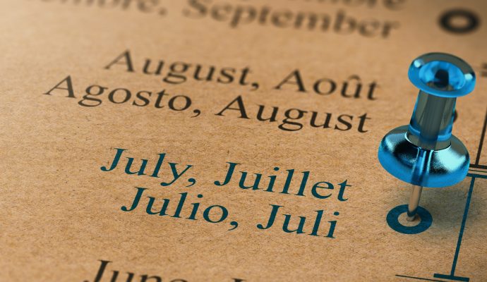 Close-up of a multilingual calendar showing the months July and August in English, French, Spanish, and German, with a blue pushpin marking July.