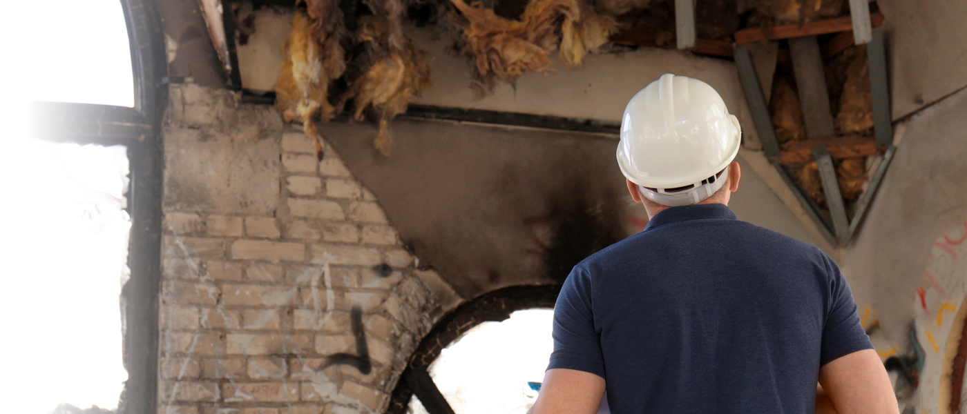 Construction worker or inspector wearing a hard hat, examining a damaged or aged industrial structure.