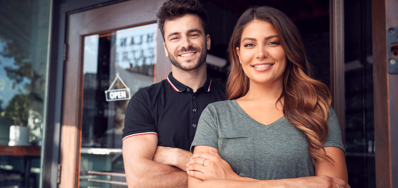 Two smiling small business owners standing confidently in front of their shop or café.