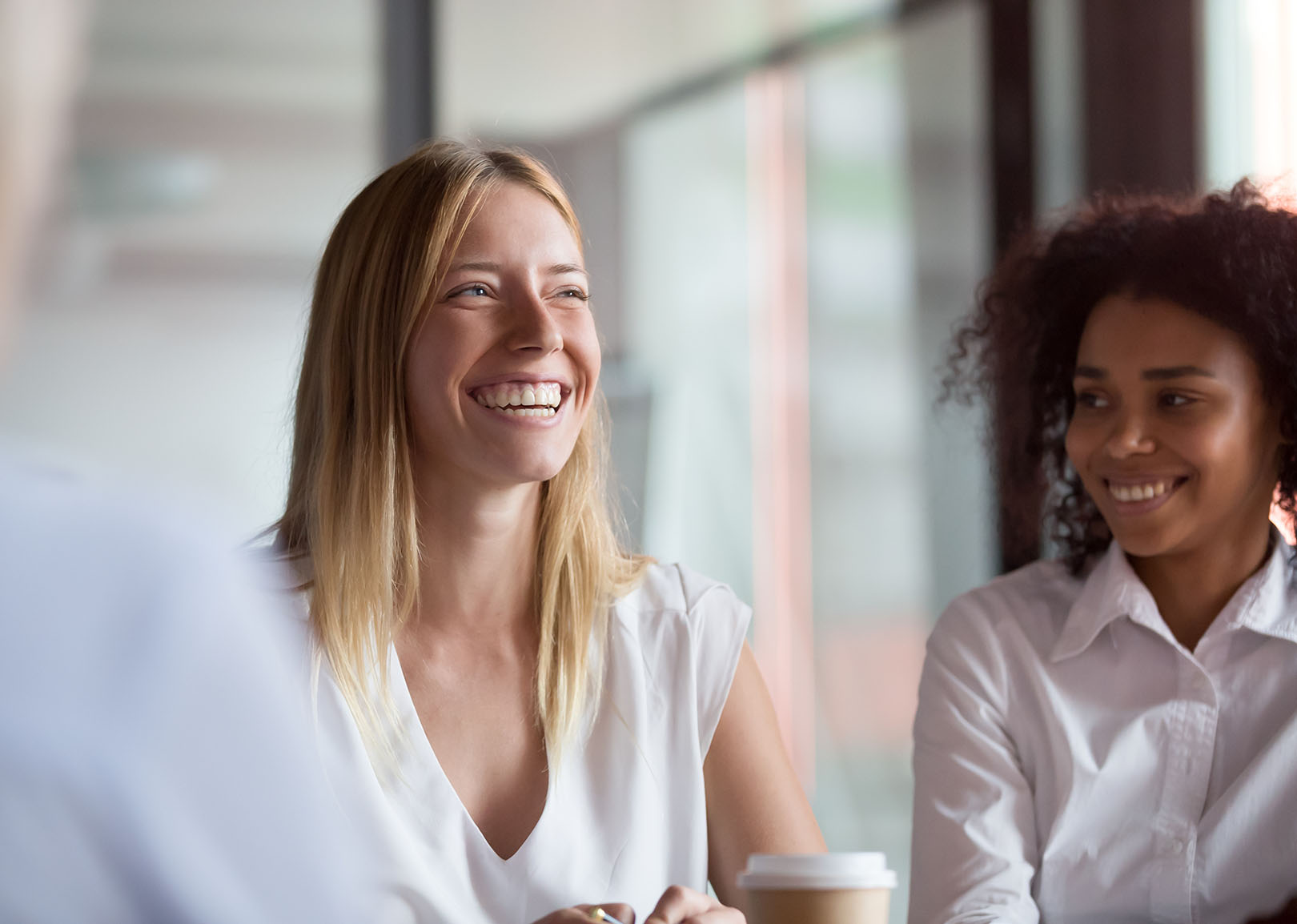 Two smiling professionals engaged in a discussion during a meeting in a bright office setting.