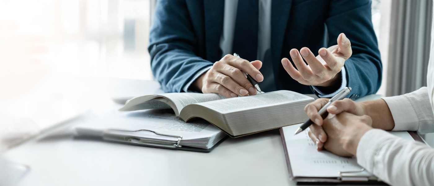 Close-up of two people discussing a document with an open book on the table in a professional setting.