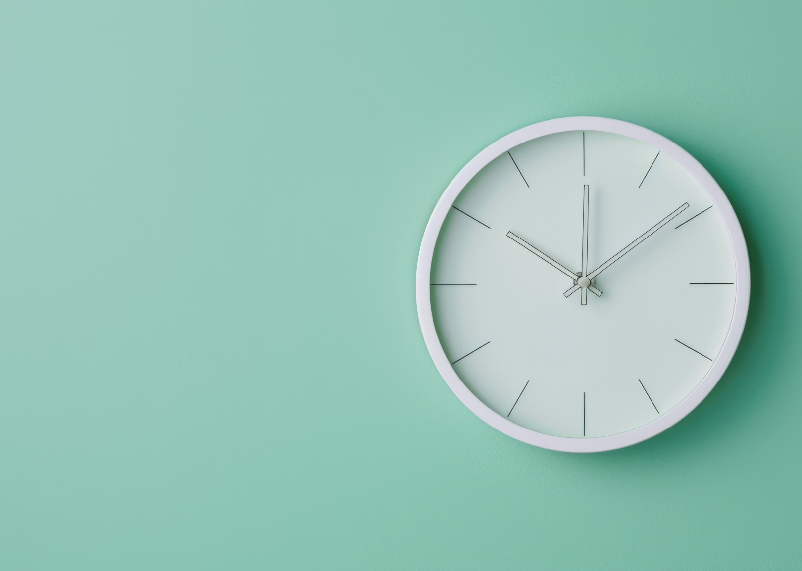 Minimalist white wall clock with thin black hands and markers on a light mint green background