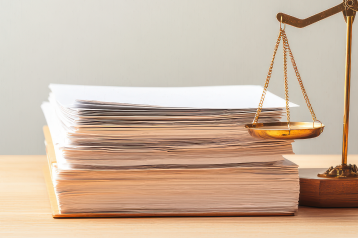 Stack of documents on a wooden desk next to a golden balance scale.