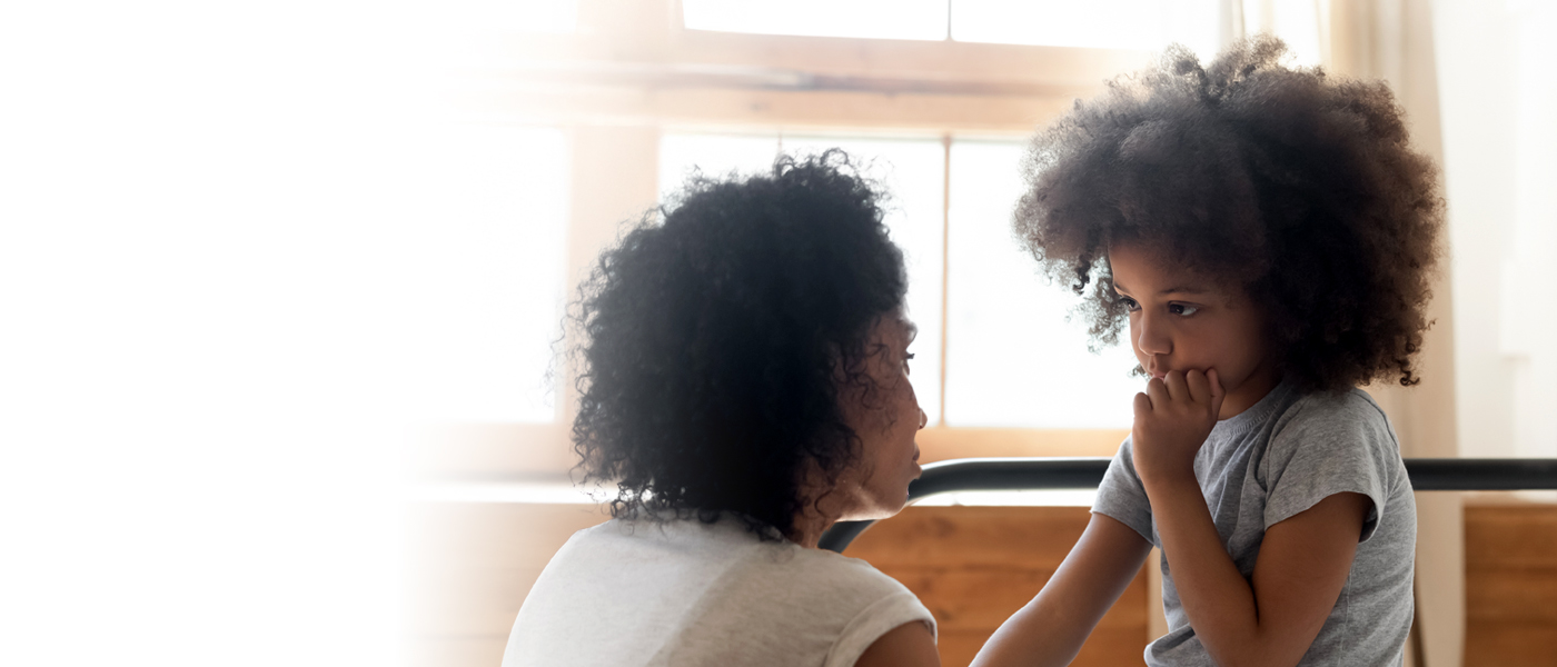 A mother comforting her young daughter in a warm, sunlit home setting.