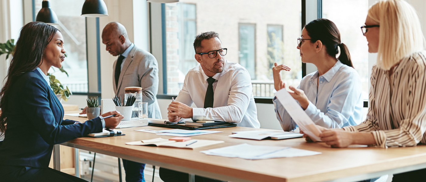 A diverse group of professionals engaged in a discussion around a conference table in a modern office setting.