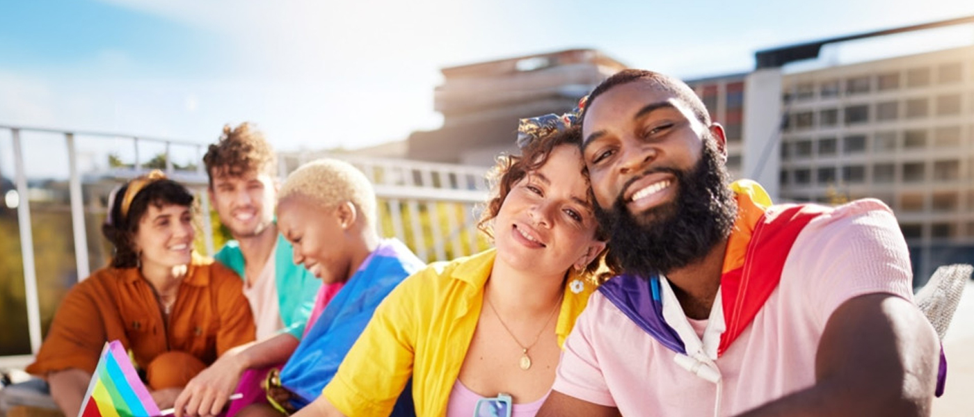 Diverse group of friends celebrating at an outdoor pride event, smiling and wearing colorful outfits.