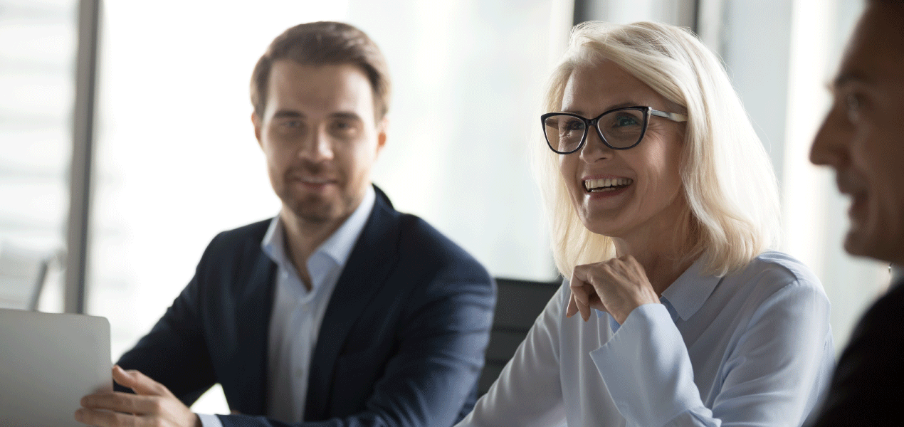 Business professionals engaged in a discussion during a meeting, with a smiling woman speaking and colleagues listening.