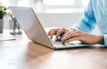 Close-up of hands typing on a laptop in a bright, modern workspace with natural light.