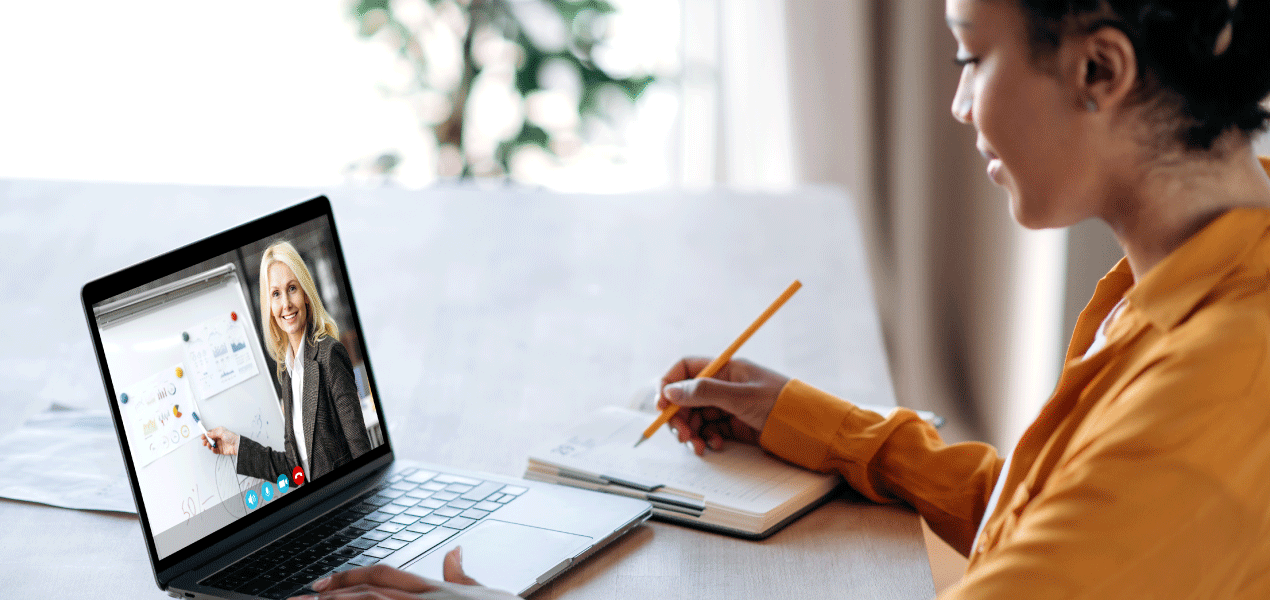 Person taking notes during an online video call on a laptop at a desk.
