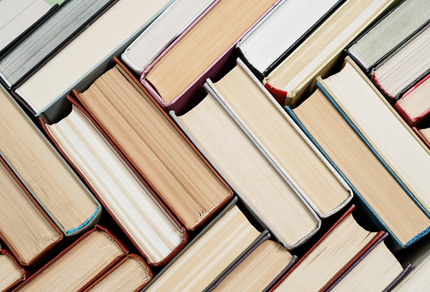 Stack of books arranged in a chevron pattern with colorful spines, placed against a neutral background.