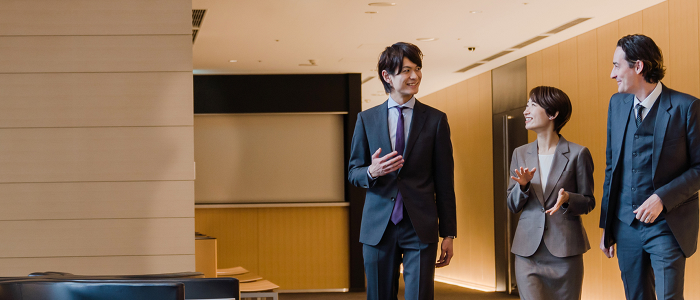 Three business professionals in formal attire walking and discussing in a modern corporate setting.