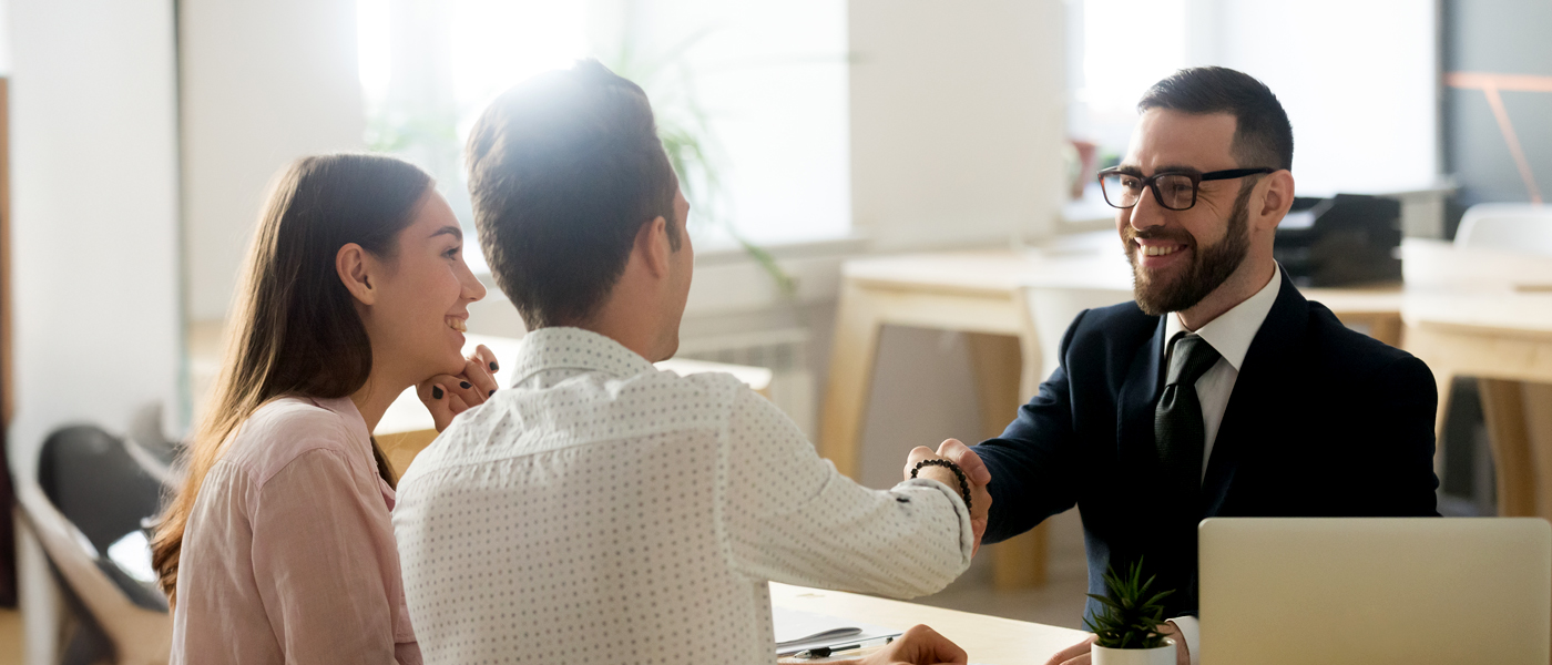 A professional handshake between a businessman and a couple in an office setting, symbolizing agreement or consultation.