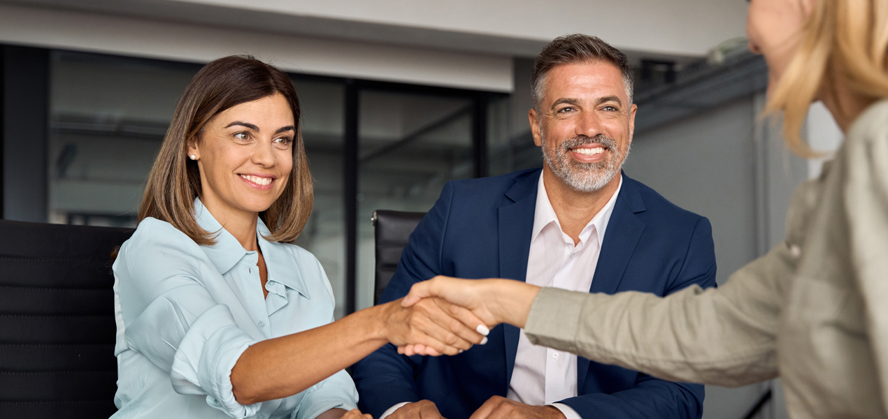 Smiling professionals in a business meeting, with two people shaking hands.