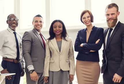 Five people in business attire standing in line smiling at the camera.