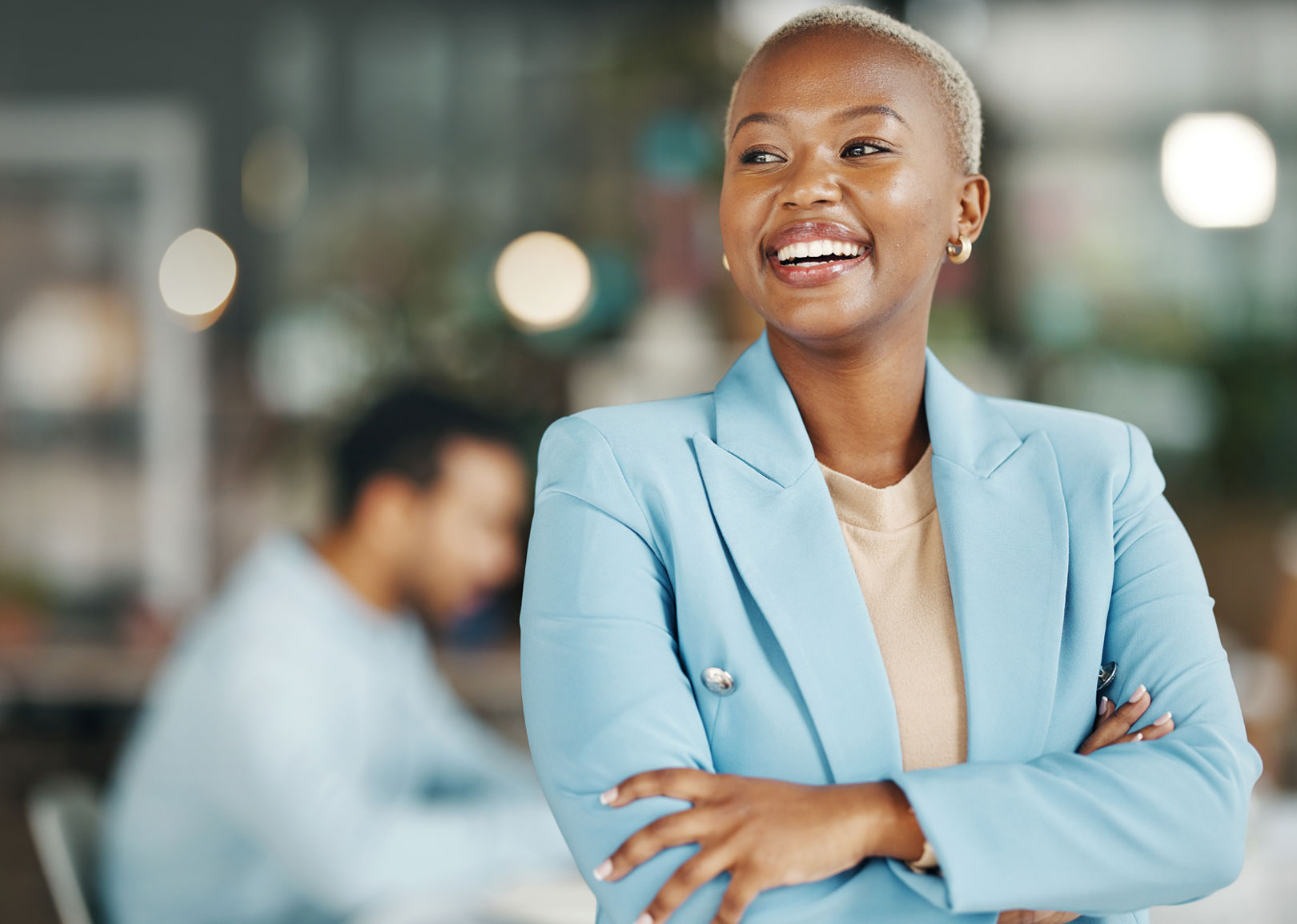 A black woman smiling and standing with arms crossed in the office.