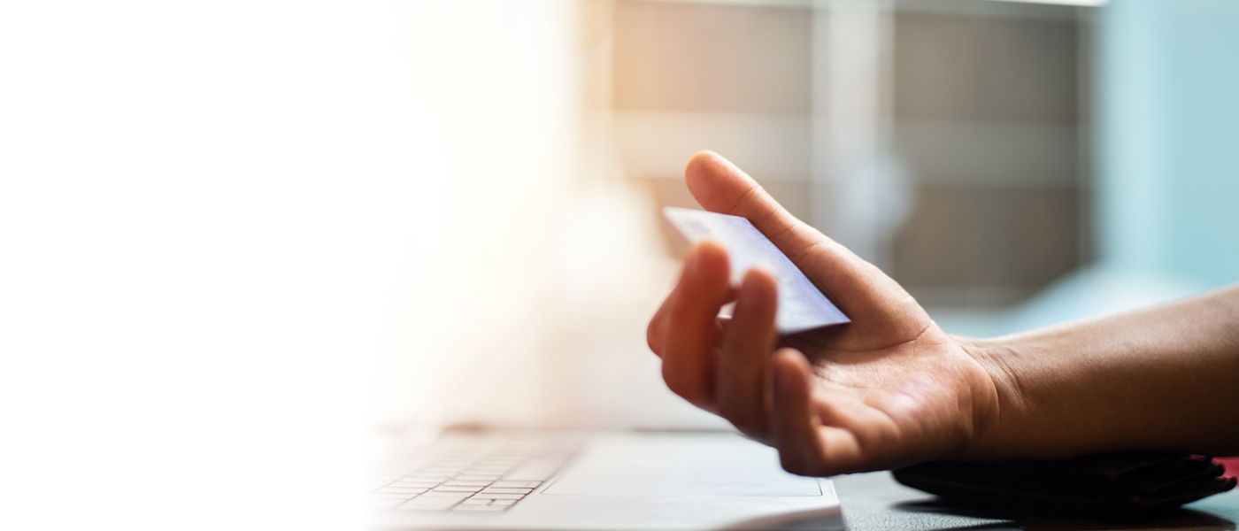 Close-up of a person holding a credit card while making an online payment or transaction.