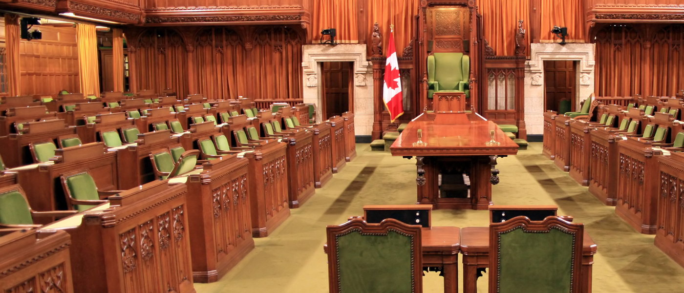 Interior of the Canadian House of Commons, featuring wooden desks, green chairs, and the Speaker's chair at the center.