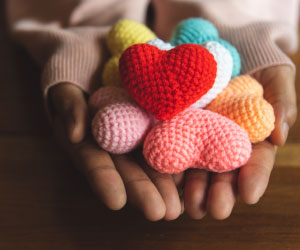 Hands gently holding a collection of colorful, knitted heart shapes, symbolizing warmth, kindness, and compassion.