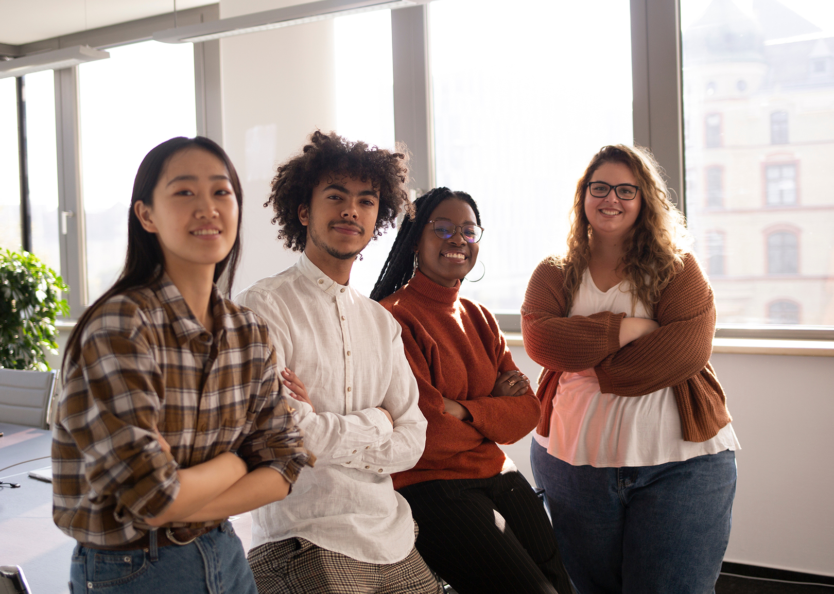 A diverse group of young professionals standing confidently in a modern office with large windows.