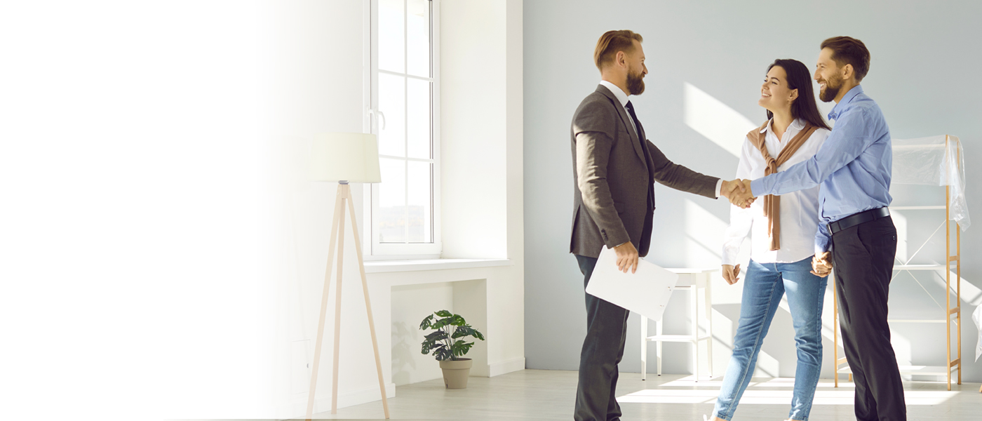 A real estate agent shaking hands with a couple in a bright, modern home, symbolizing a successful deal.