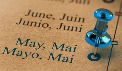 A close-up of a calendar or timeline showing the months "June" and "May" in multiple languages, with a blue pushpin marking a specific point on the timeline