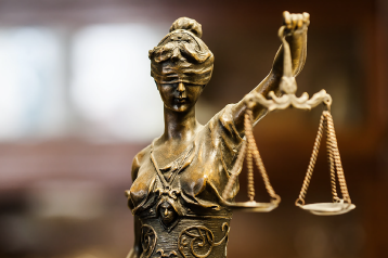 Close-up of a bronze Lady Justice statue holding scales, with a blurred background.