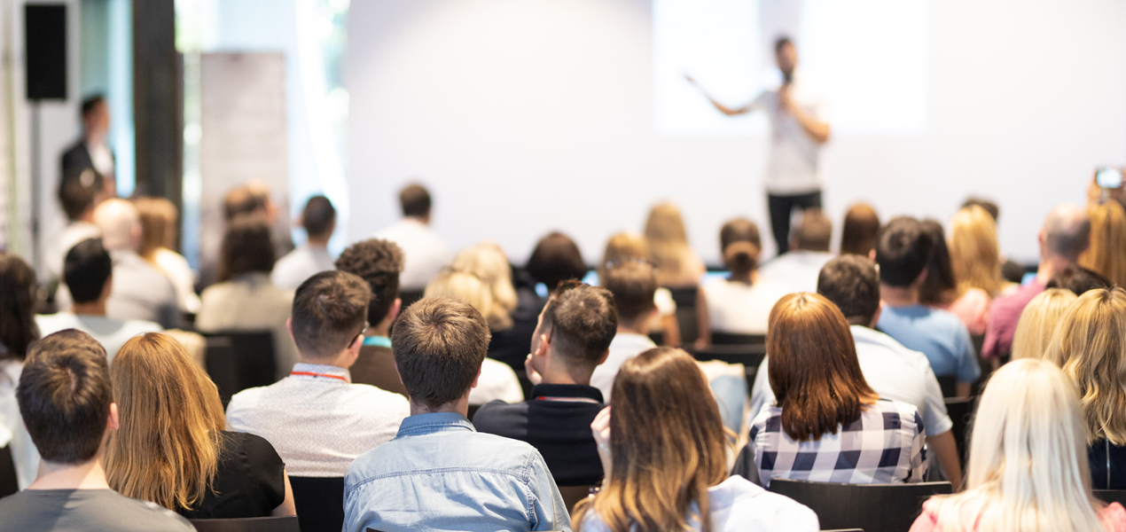 Audience listening to a speaker during a professional seminar or training session in a bright modern conference room.