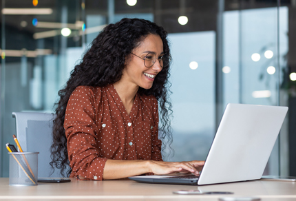 Woman smiling while working on a laptop in a modern office.