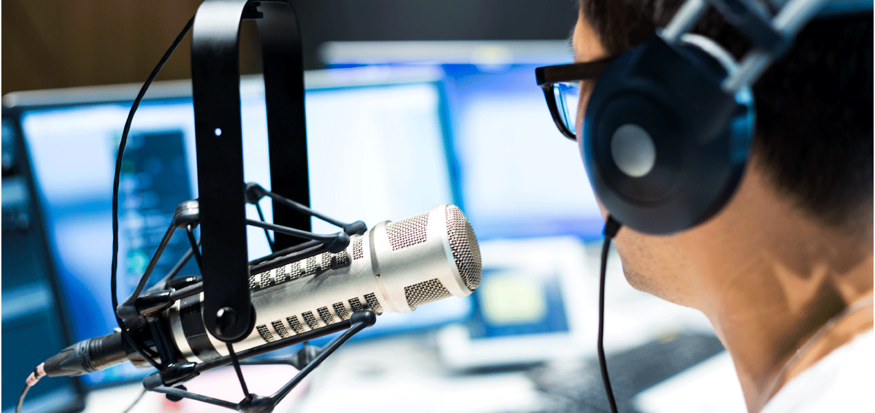 Radio broadcaster wearing headphones, speaking into a professional microphone in a recording studio.