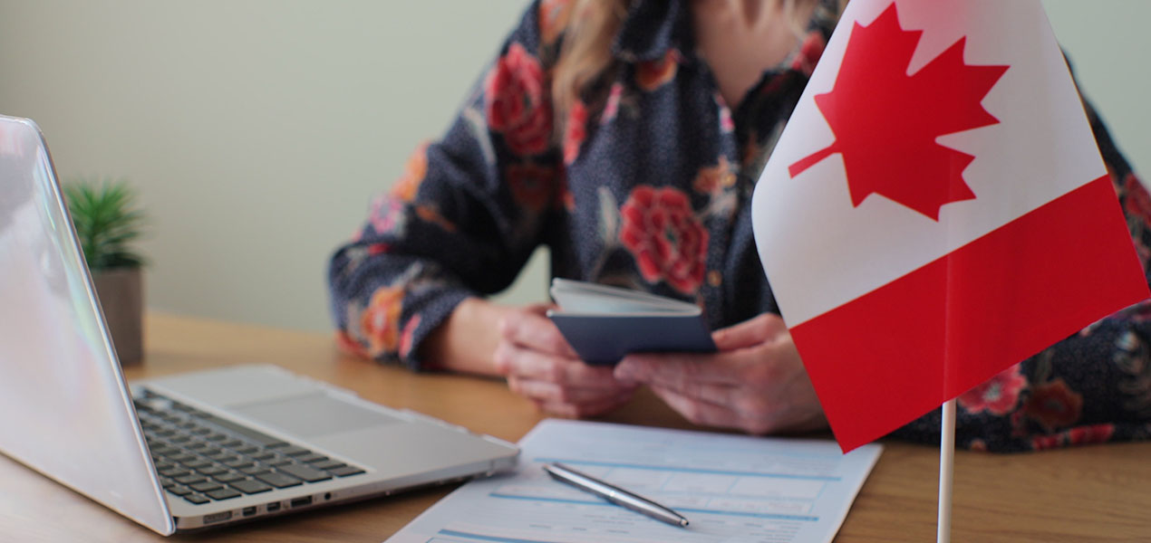 Individual completing an immigration visa application with a Canadian flag in the foreground.