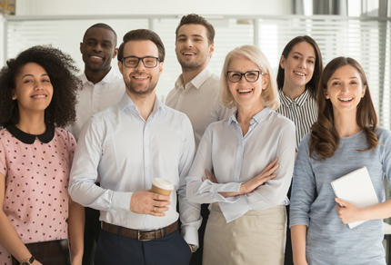Diverse group of smiling business professionals standing together in a bright office, representing teamwork, collaboration, and workplace diversity.