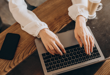 Person typing on a laptop while seated at a wooden desk.