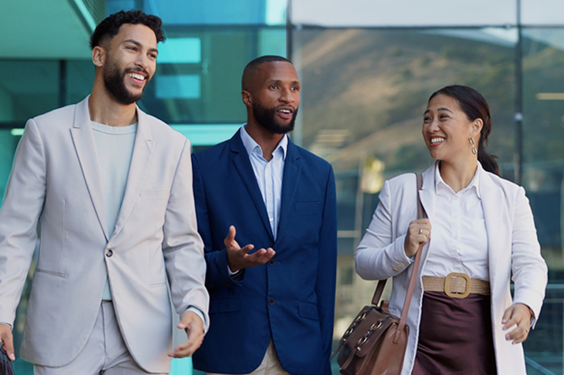 Three professionally dressed individuals walking and conversing outside a modern glass building