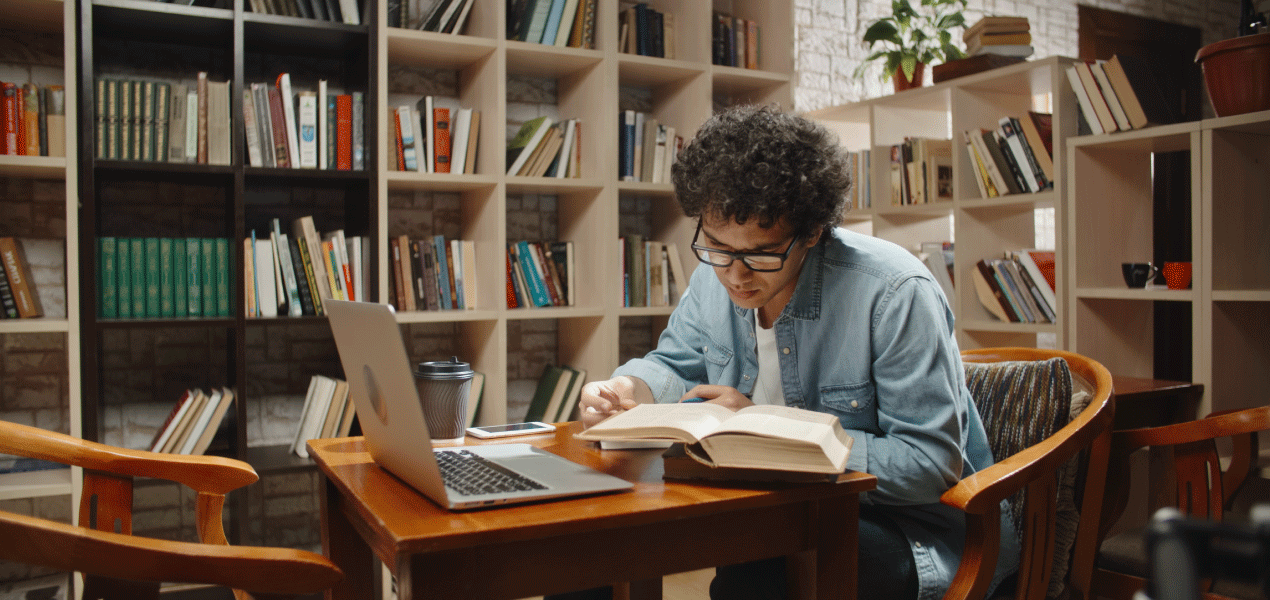Law student studying with a laptop and books at a table in a university library.