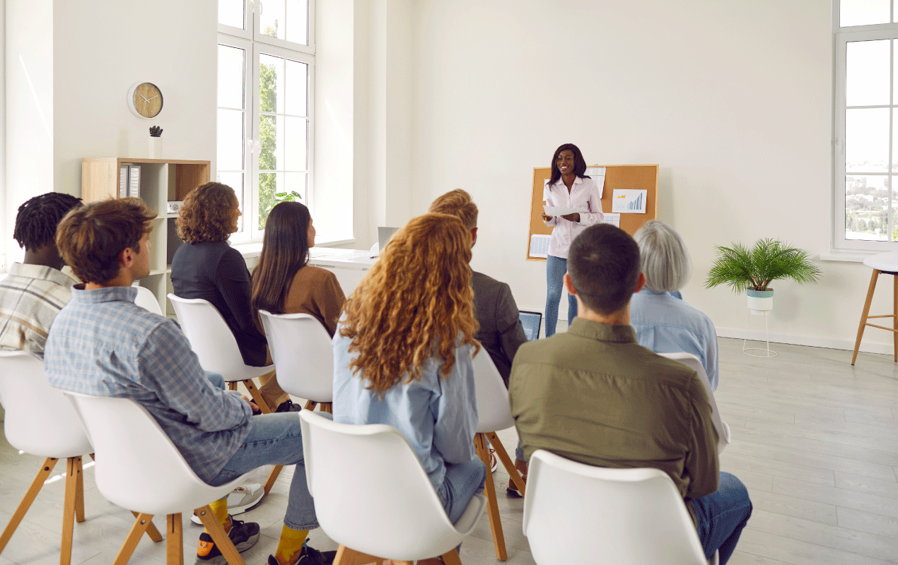 Presenter leading a community legal information session for a seated, diverse audience in a bright, sunlit room.