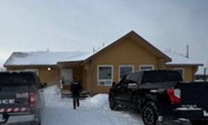 photo of rustic cottage with snowy roof and snowy lawn with two pickup trucks out front and a walking figure approaching door