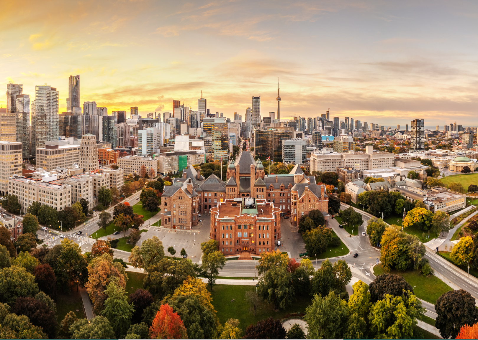 Aerial view of Queen's Park building surrounded by greenery, with the Toronto city skyline and CN Tower in the background at sunset.